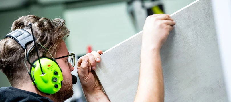 Mitarbeiter mit Hörschutz, kontrolliert eine Holzplatte für Frontenmöbel