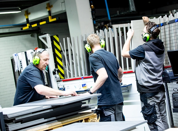 Drei Mitarbeiter verarbeiten Fronten an einer Maschine